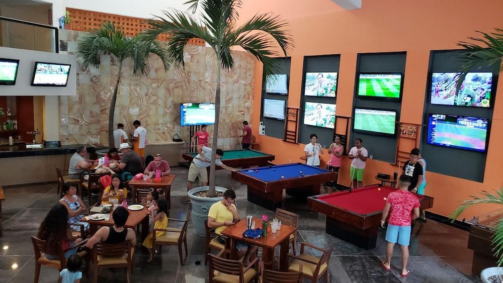 แกรนด์ โอเอซิส ปาล์ม ออล อินคลูซีฟ Hotel แคนคูน ภายนอก รูปภาพ The photo shows a lively recreational area inside a building, likely a bar or game room. There are several pool tables, one blue and one red, where people are playing or waiting for their turn. 

Around the area, groups of people are seated at tables