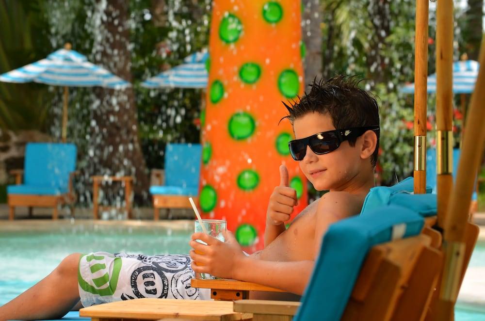 แกรนด์ โอเอซิส ปาล์ม ออล อินคลูซีฟ Hotel แคนคูน ภายนอก รูปภาพ The photo shows a young boy relaxing by a pool. He is wearing sunglasses and has a thumbs-up gesture, signaling enjoyment. He appears to be lounging on a chair, holding a drink in a glass. In the background, there is a bright and colorful structure w