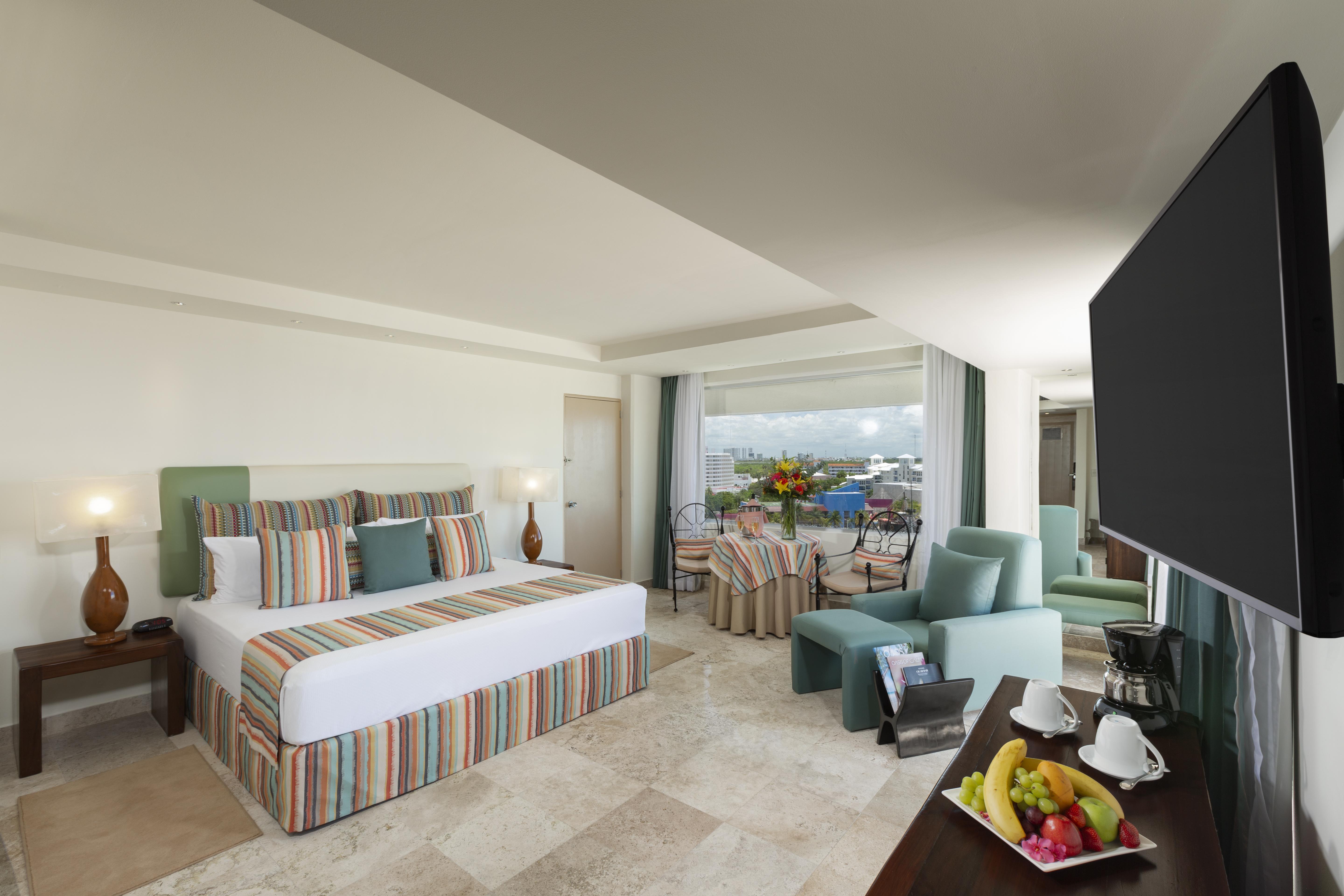 แกรนด์ โอเอซิส ปาล์ม ออล อินคลูซีฟ Hotel แคนคูน ภายนอก รูปภาพ The photo shows a spacious hotel room with modern decor. It features a large bed with a striped duvet and decorative pillows, flanked by two lamps. There are comfortable seating areas with light green chairs and a small table. A balcony can be seen i
