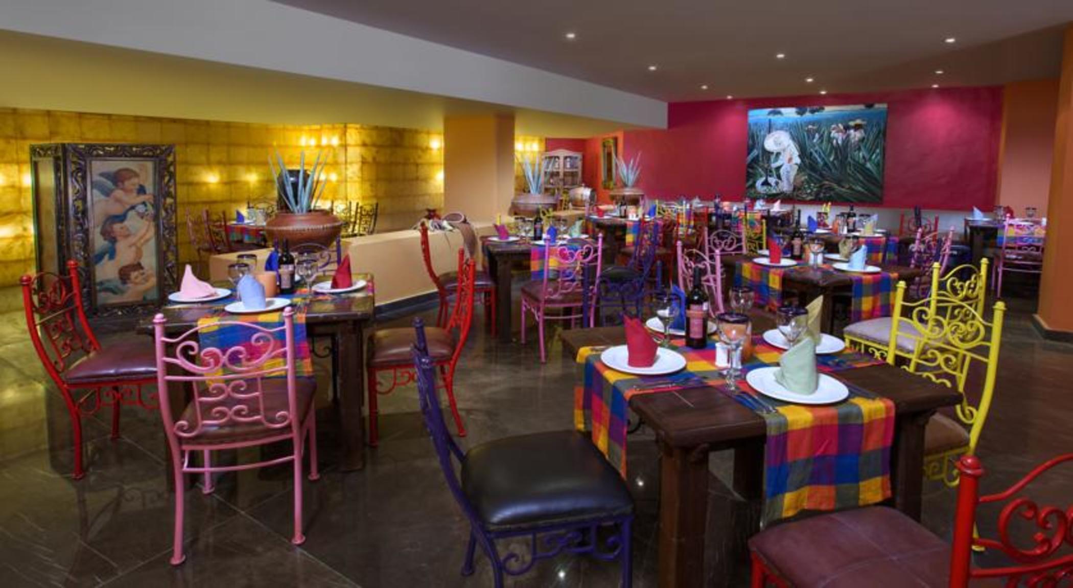 แกรนด์ โอเอซิส ปาล์ม ออล อินคลูซีฟ Hotel แคนคูน ภายนอก รูปภาพ The photo shows a vibrant and colorful restaurant interior. There are several tables arranged with multicolored tablecloths, each adorned with plates and decorative napkins. The chairs are also colorful, featuring a mix of pink, purple, and metal des