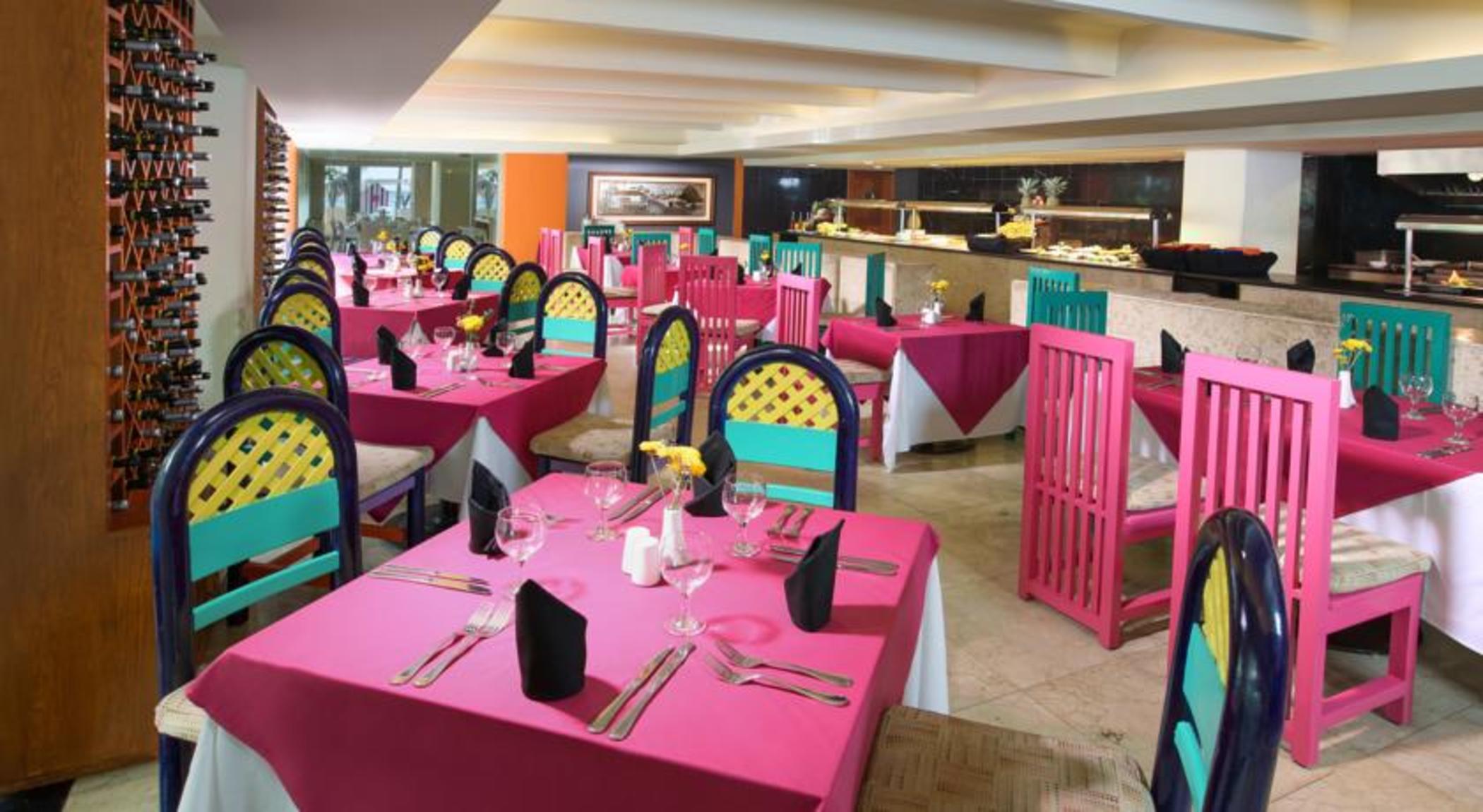 แกรนด์ โอเอซิส ปาล์ม ออล อินคลูซีฟ Hotel แคนคูน ภายนอก รูปภาพ The photo shows a vibrant restaurant interior featuring colorful decor. There are multiple tables covered with bright pink tablecloths. Each table is equipped with utensils, napkins, and a small centerpiece, possibly a flower. The chairs are painted 