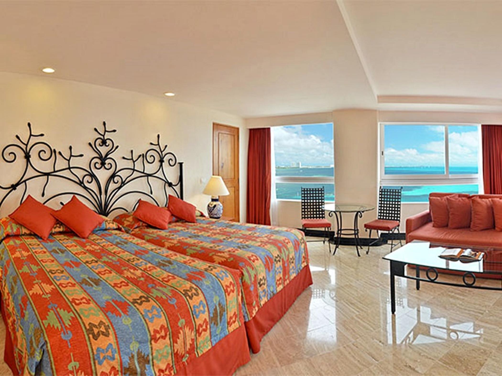 แกรนด์ โอเอซิส ปาล์ม ออล อินคลูซีฟ Hotel แคนคูน ภายนอก รูปภาพ The photo shows a spacious hotel room featuring two beds with colorful patterned bedding. The walls are decorated with a decorative iron headboard. There are large windows that provide a view of the ocean and a bright, sunny sky. The room is warmly l