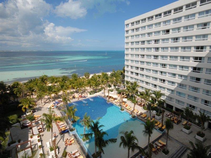 แกรนด์ โอเอซิส ปาล์ม ออล อินคลูซีฟ Hotel แคนคูน สิ่งอำนวยความสะดวก รูปภาพ The image shows a luxurious hotel resort situated by the ocean. In the foreground, there is a large swimming pool surrounded by palm trees and sun loungers, creating a relaxing atmosphere for guests. Beyond the pool, the beach and ocean can be seen, 