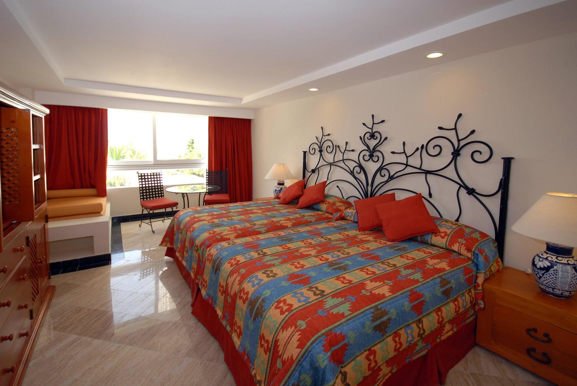 แกรนด์ โอเอซิส ปาล์ม ออล อินคลูซีฟ Hotel แคนคูน ภายนอก รูปภาพ The photo shows a hotel room with a bright and colorful design. It features two beds with ornate, decorative headboards. The bedding has a vibrant pattern that includes various colors. There are red curtains covering the windows, which allow natural 